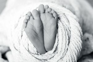 A close-up black and white photograph of tiny newborn baby feet wrapped in soft white fabric.