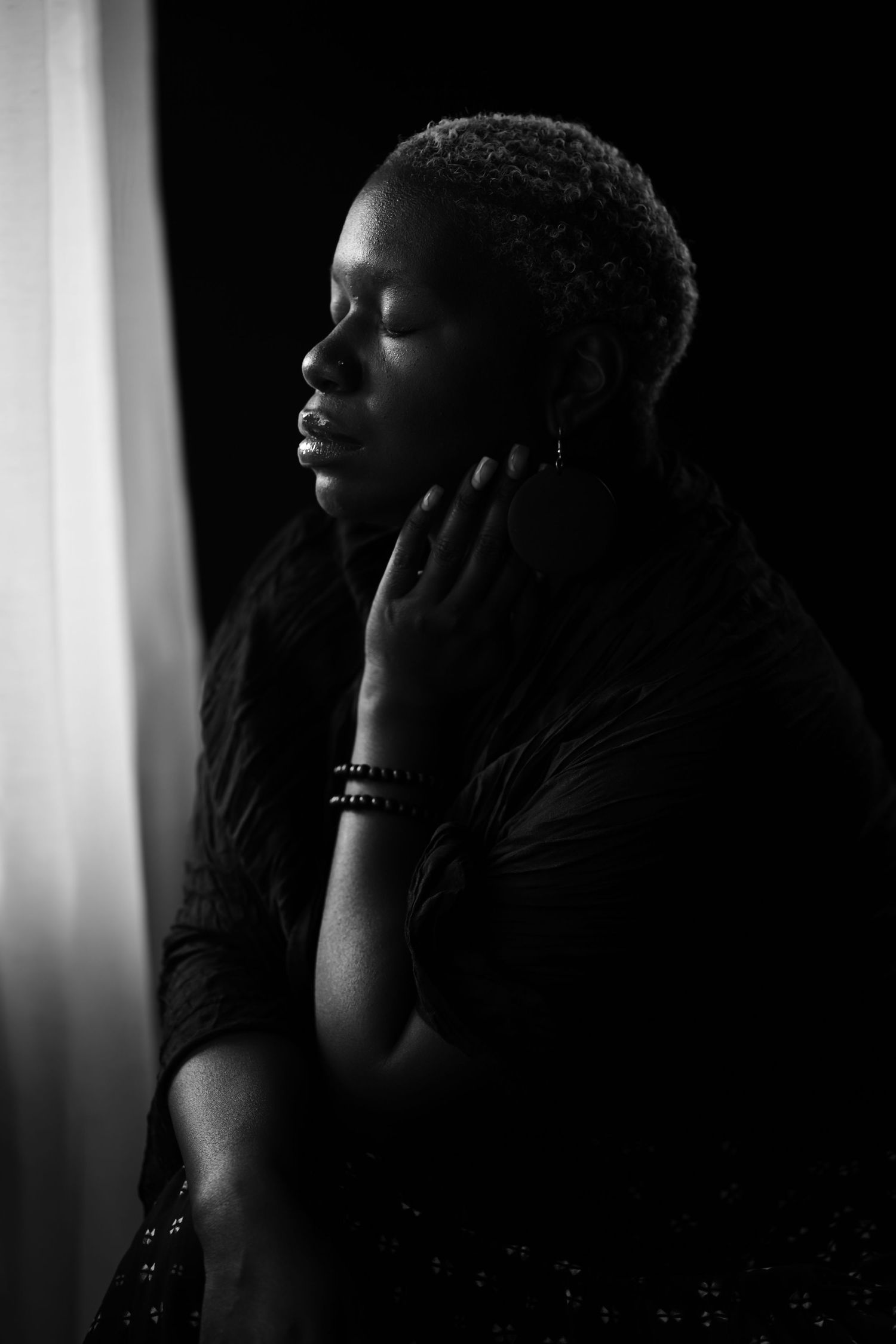 Artistic black and white portrait showcasing contemplative pose against window light.