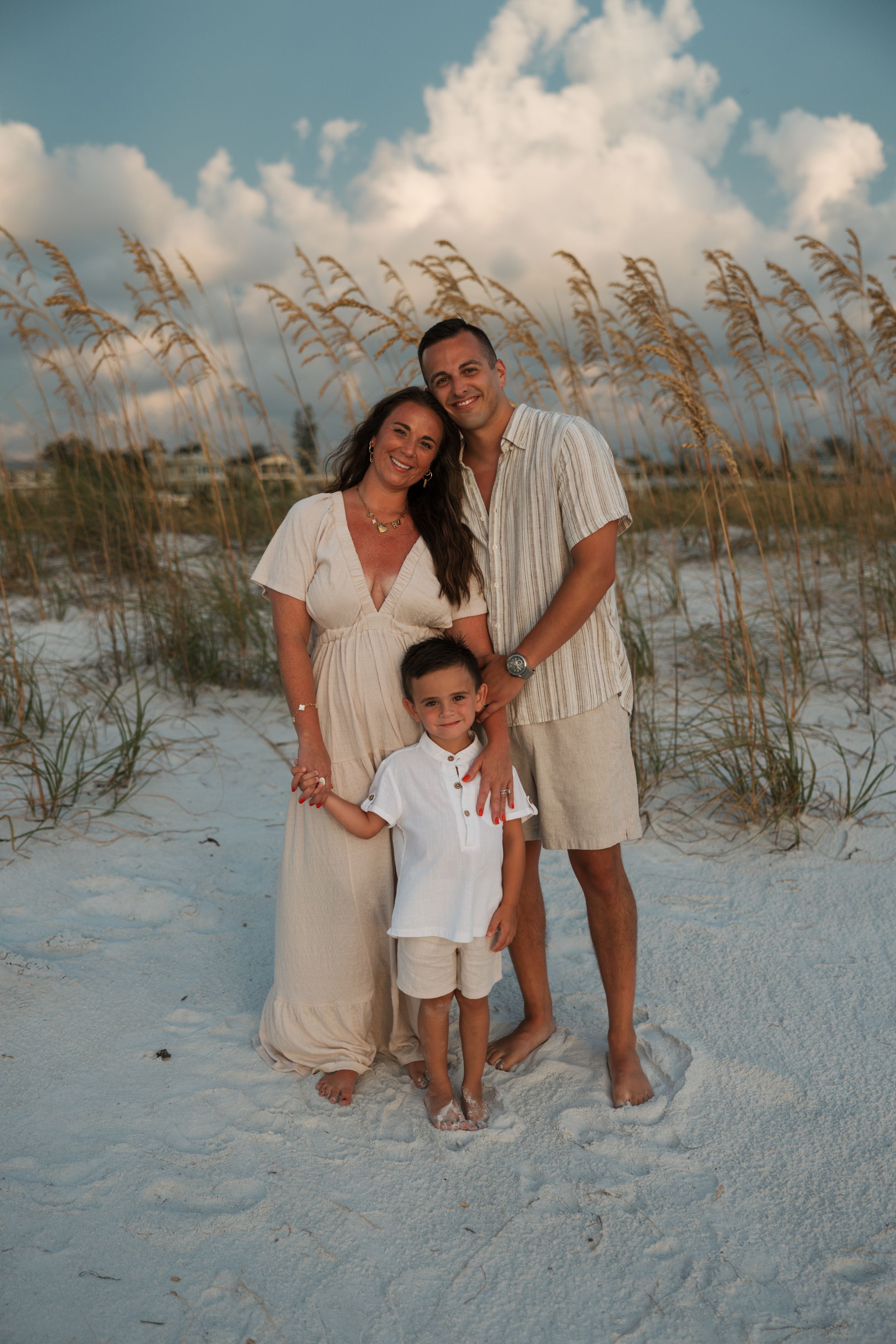 Family stands together on white sand beach with sea oats at sunset.