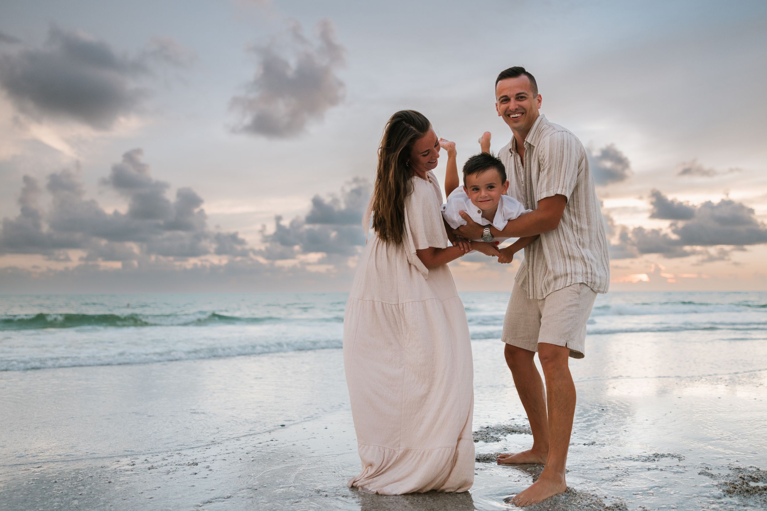 Family in white outfits sharing a moment on beach at sunset.