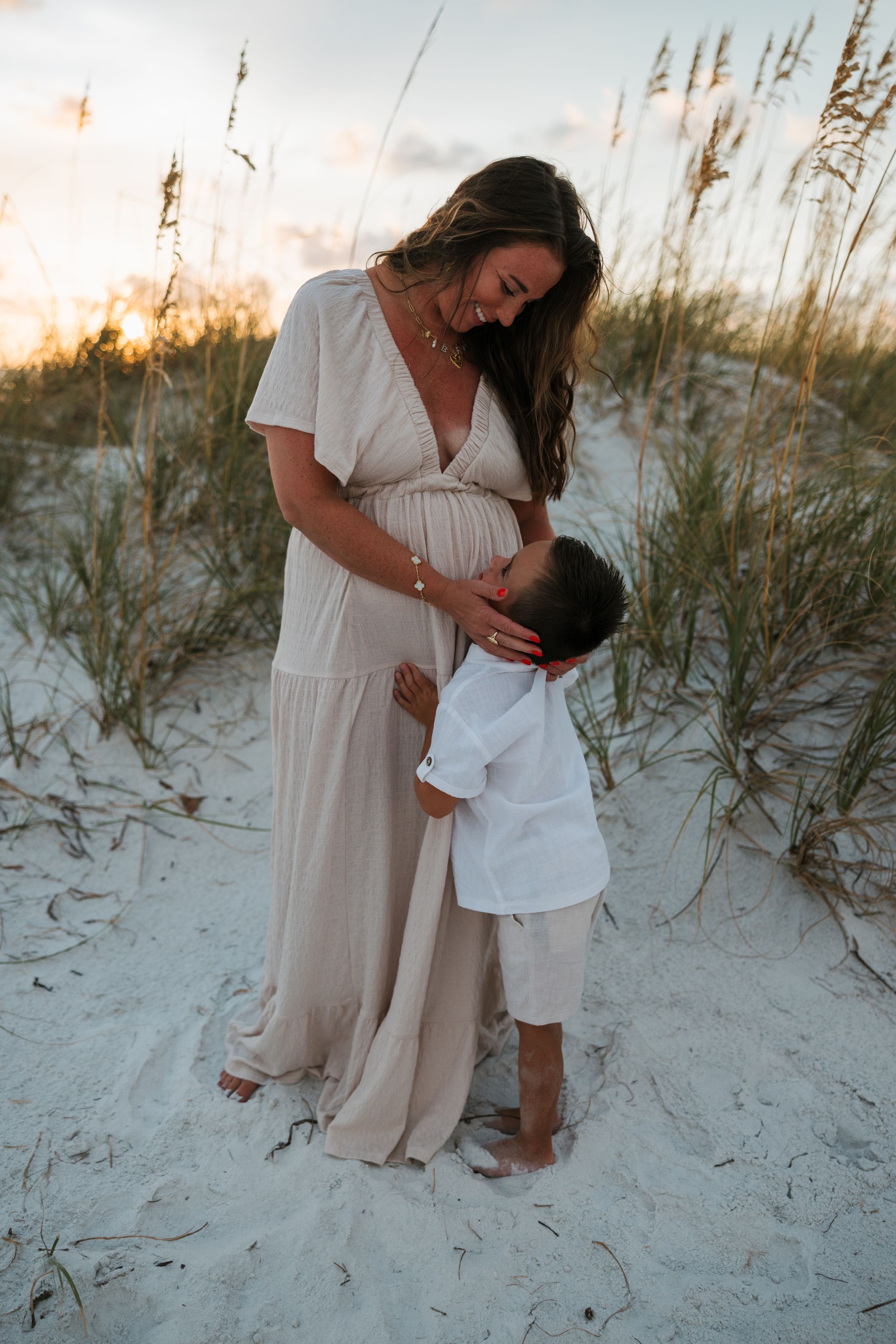 Tender moment between parent and child on sandy beach with sea oats at sunset.
