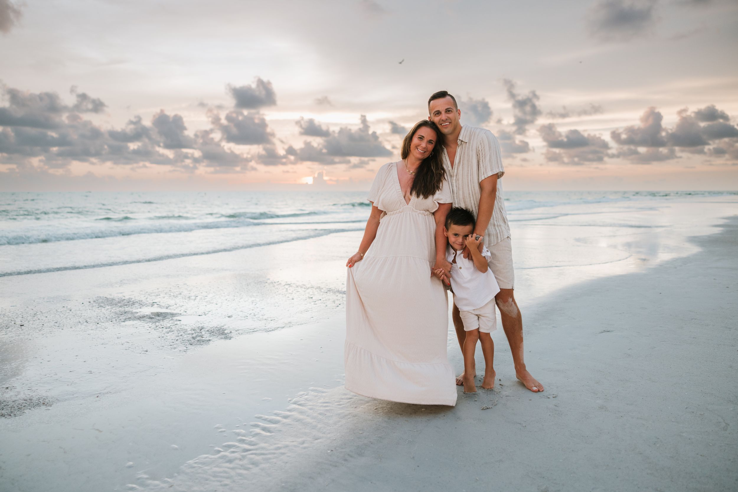 Family of three walking along ocean shore during golden hour.