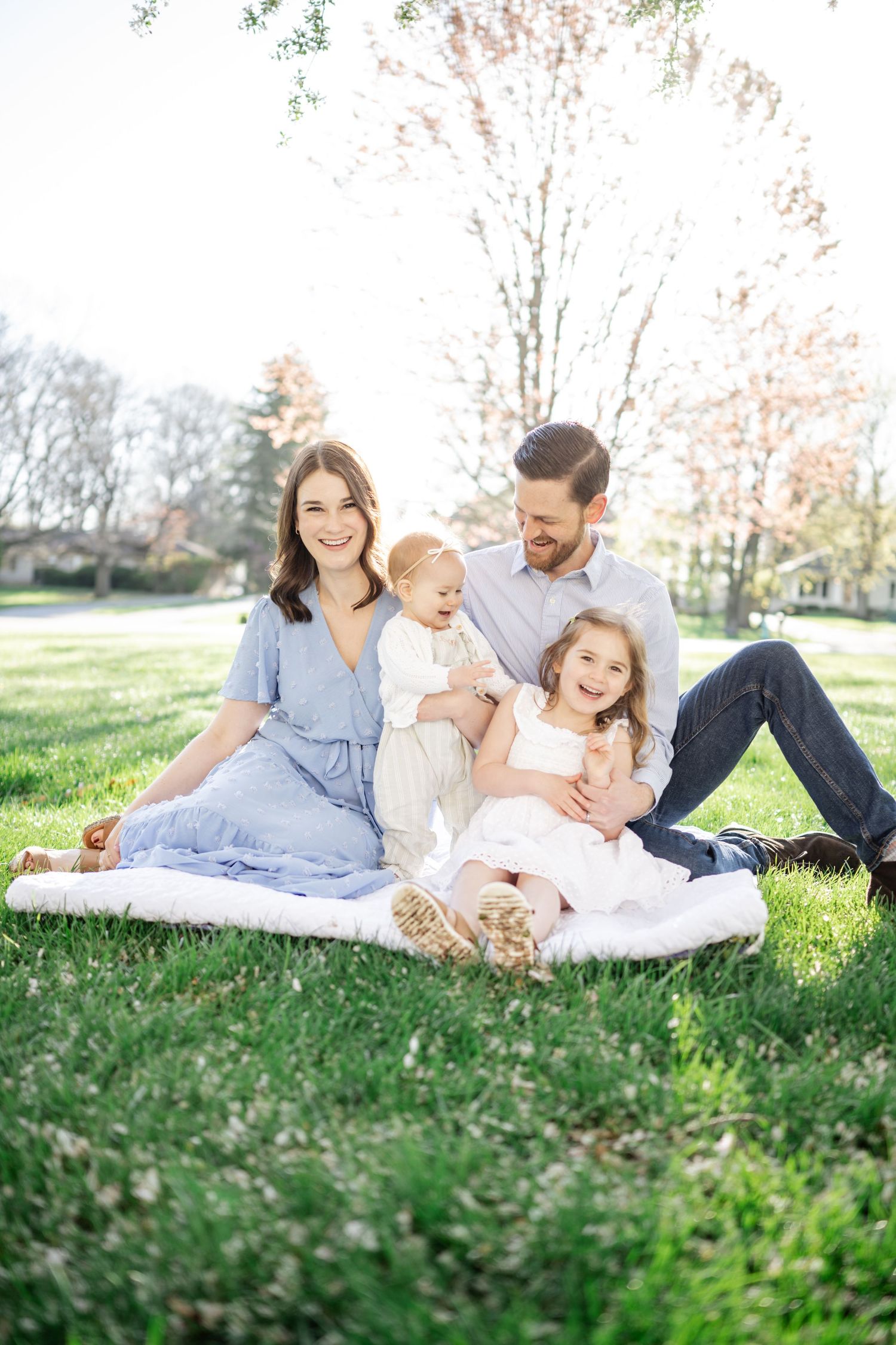 family photographer westfield, family sits on white blanket and mom smiles at camera while kids and dad smile