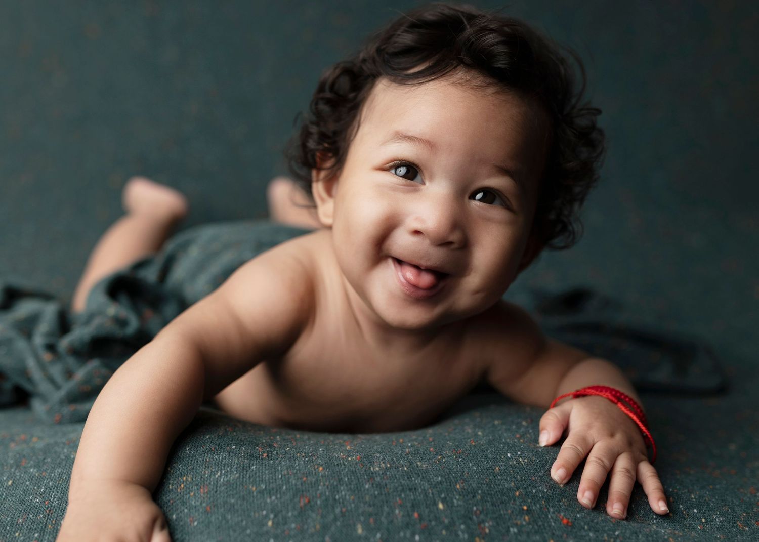 Candid portrait of laughing baby on teal background.