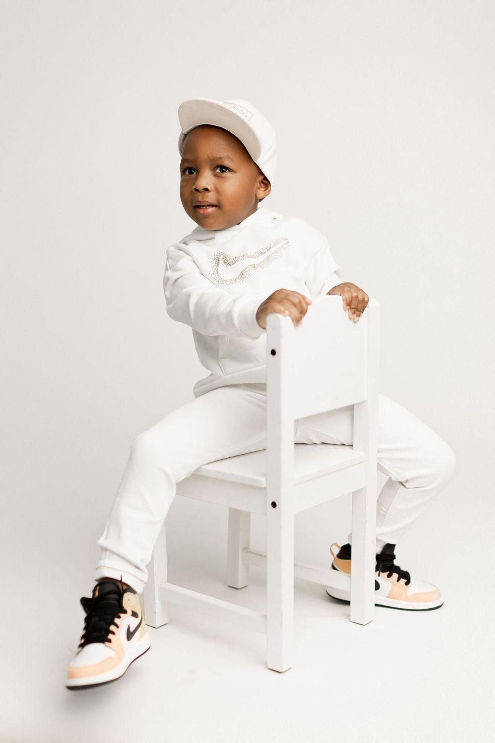 Stylish youth in all-white outfit sitting backwards on chair against light background.
