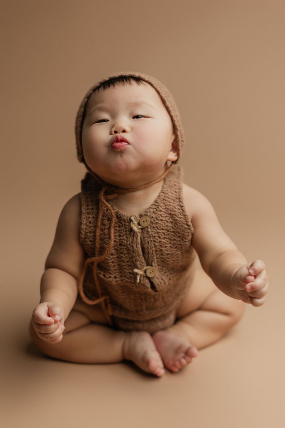 Baby in brown knit outfit makes playful expression during studio photoshoot.