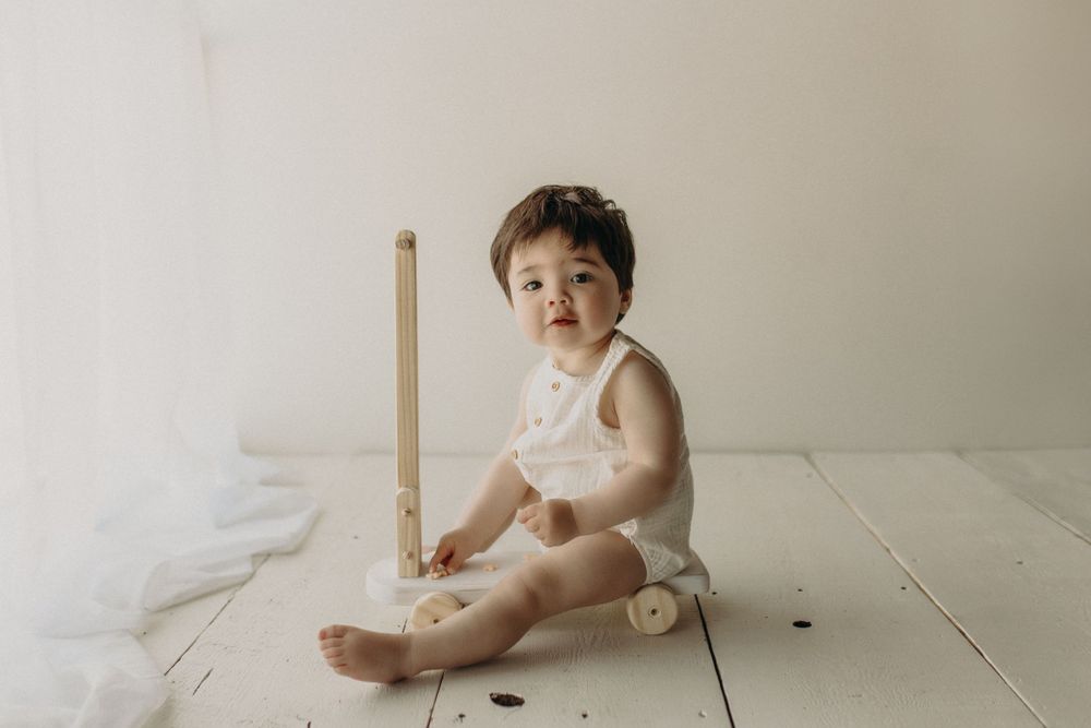 Baby in white outfit sits on wooden floor with measuring stick.