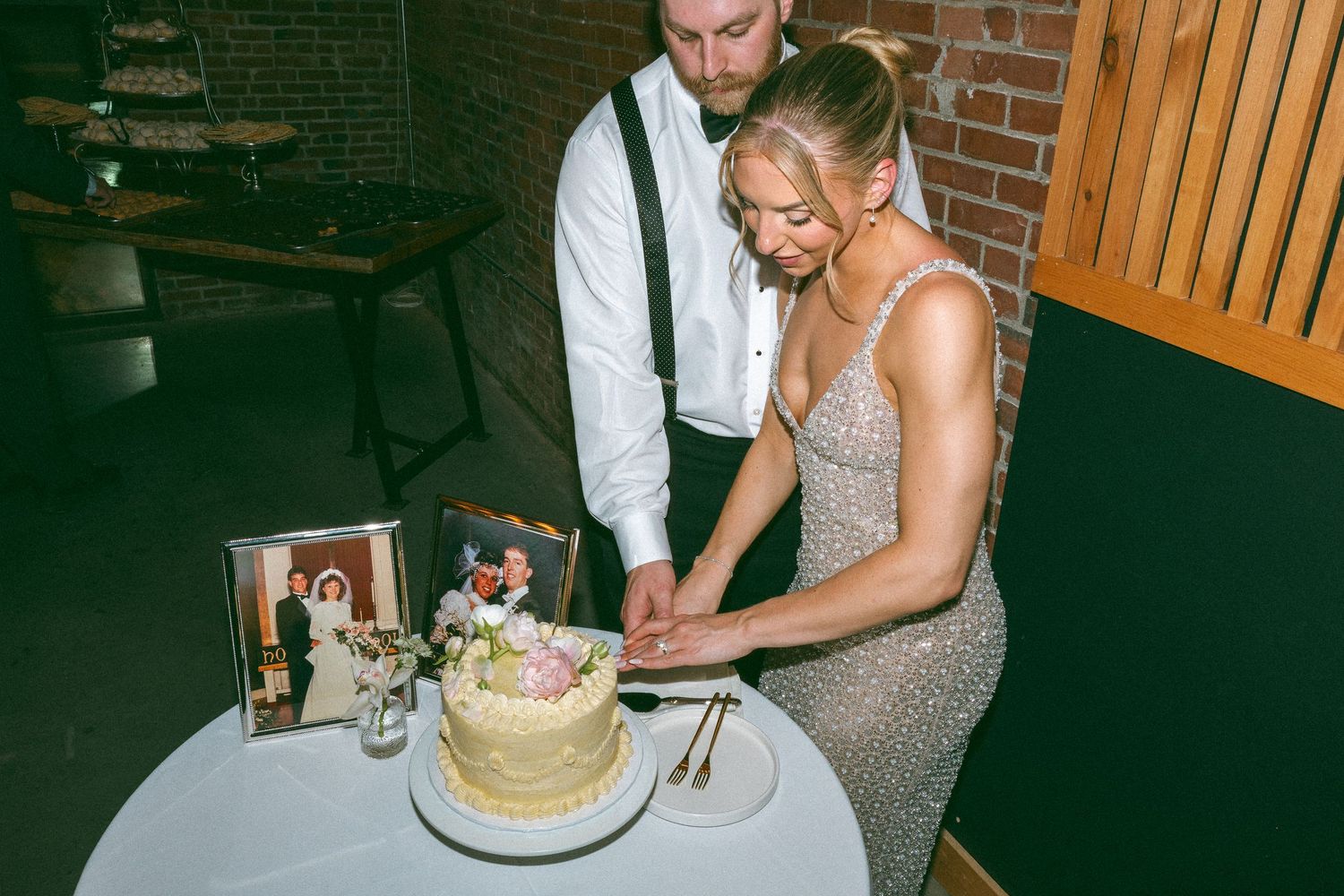 Bride and groom cutting their floral wedding cake at a reception, with a framed photo displayed on the table.