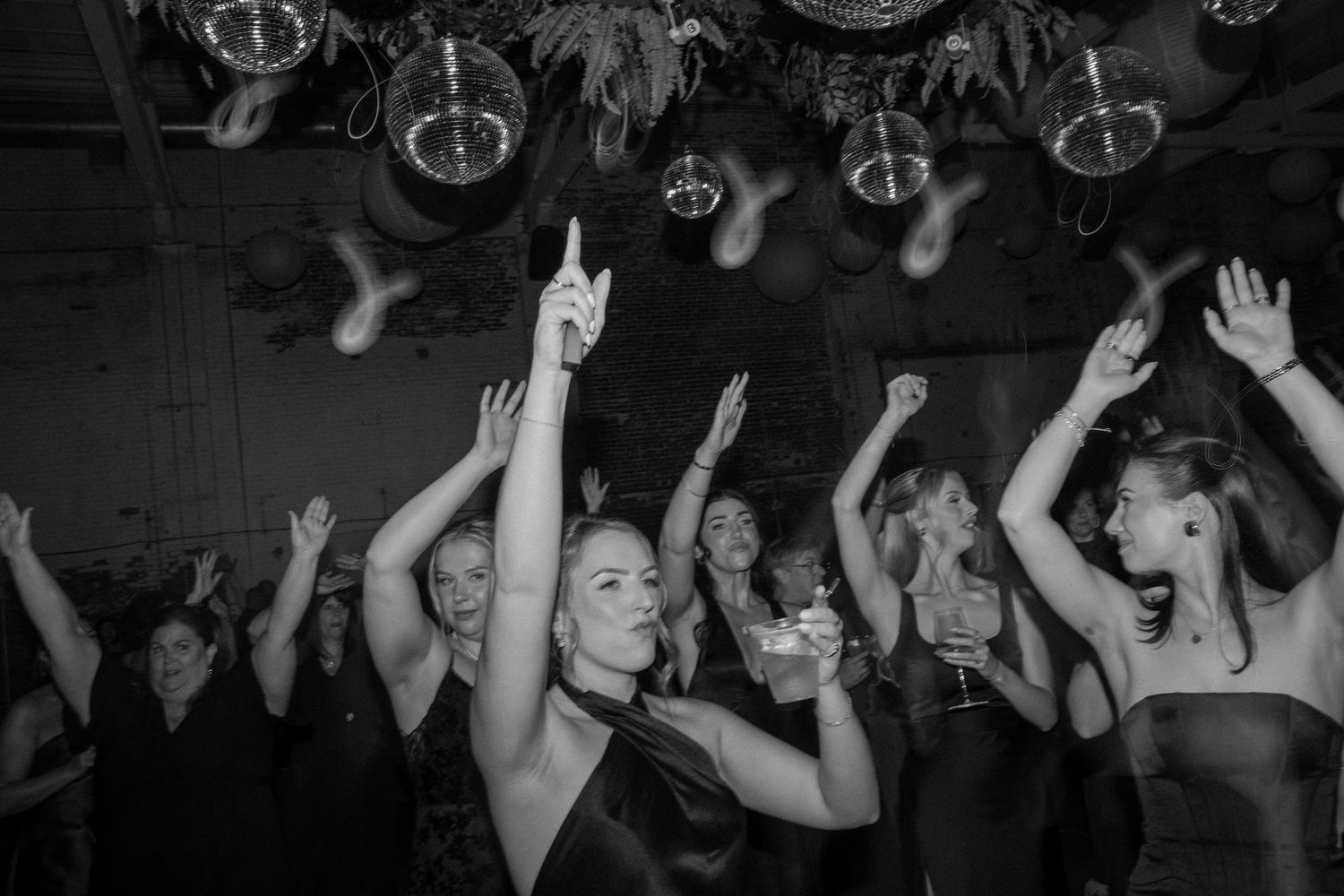 Black and white photo of women dancing and celebrating at a party under disco balls.