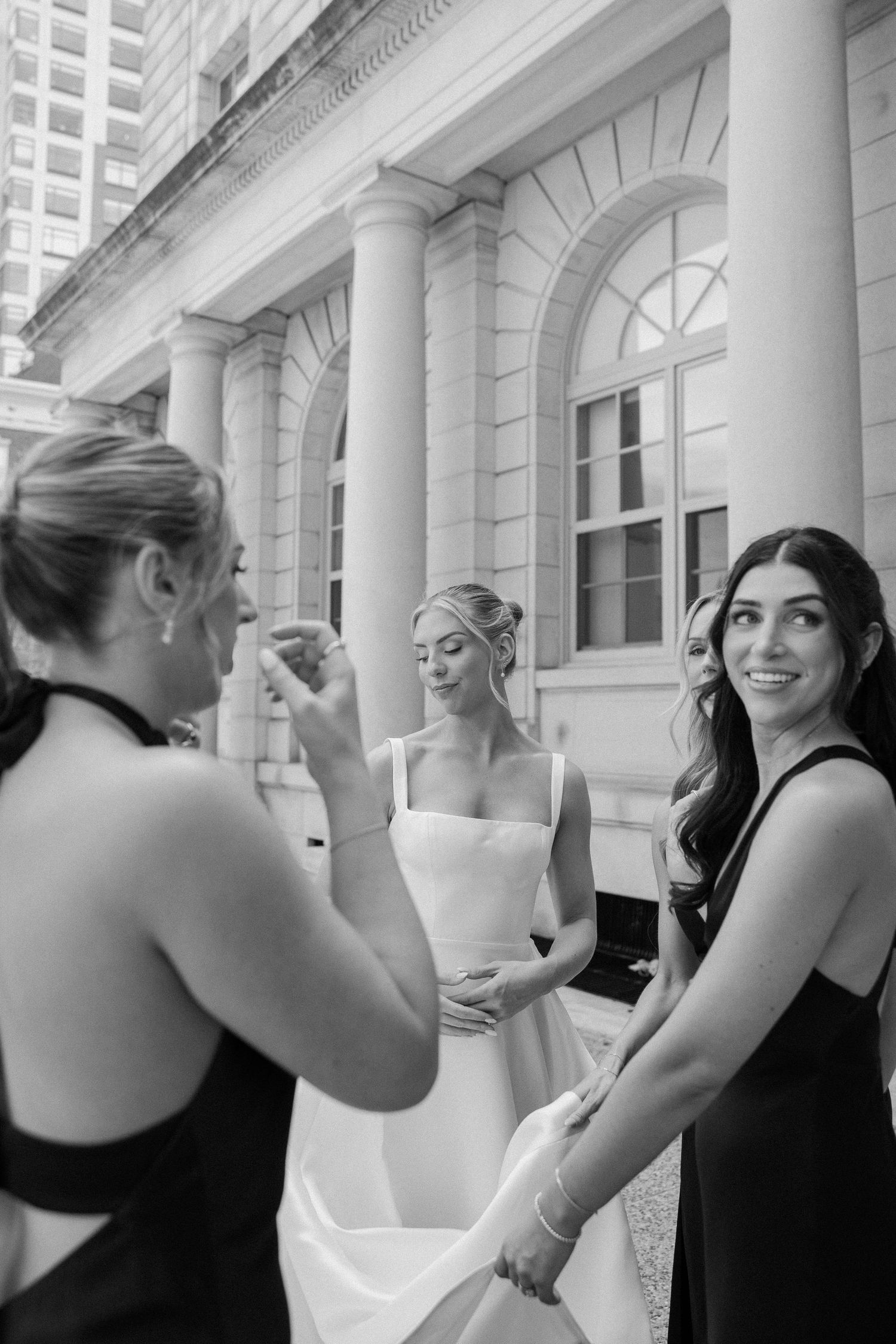 Black and white photo of a bride with two bridesmaids in black dresses outside a classical building.