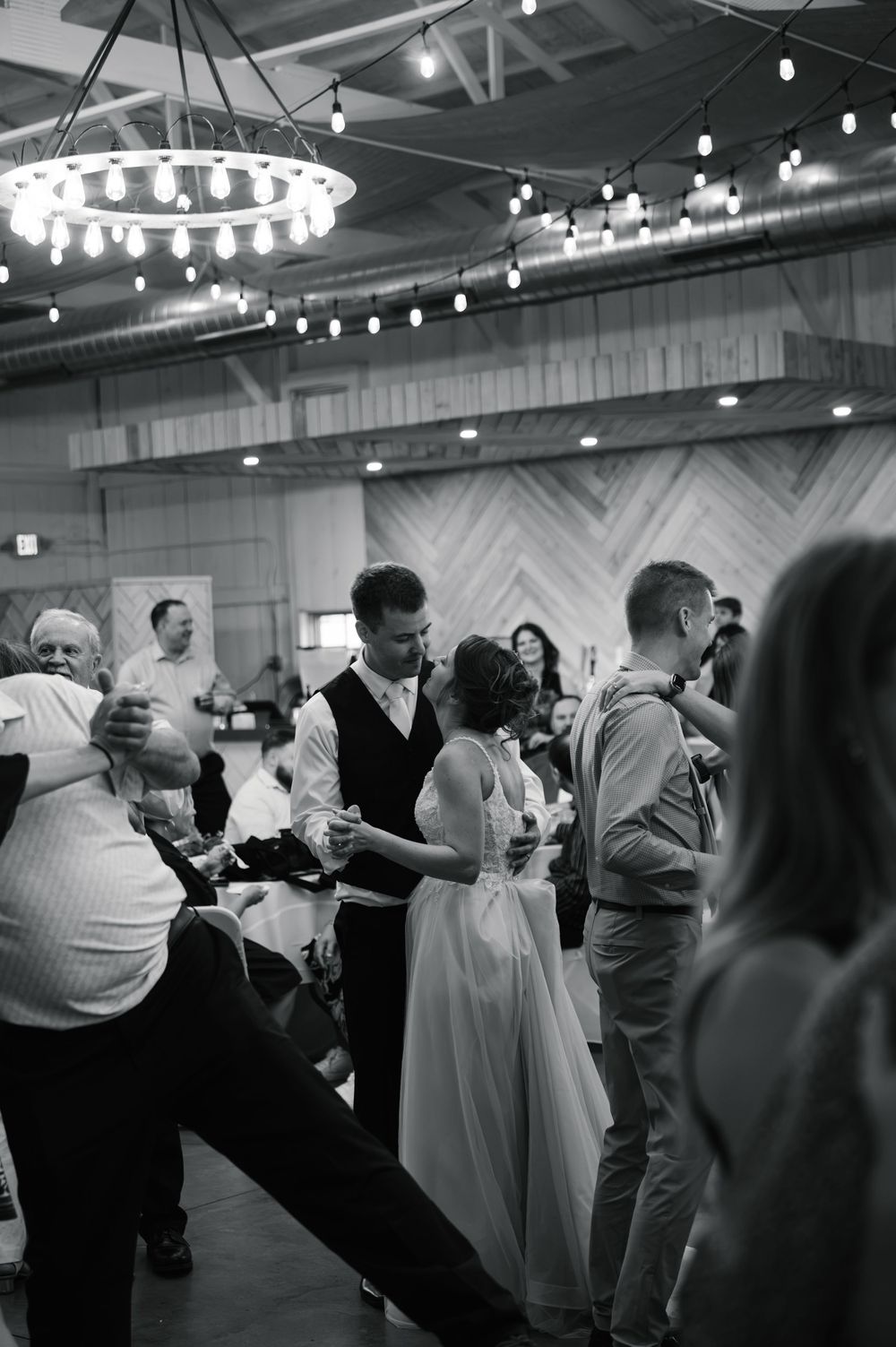 Black and white photo of a bride and groom sharing a dance at their wedding reception in a rustic venue.