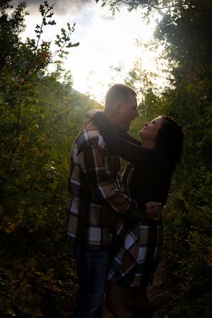 Romantic backlit couple embracing among trees at sunset.