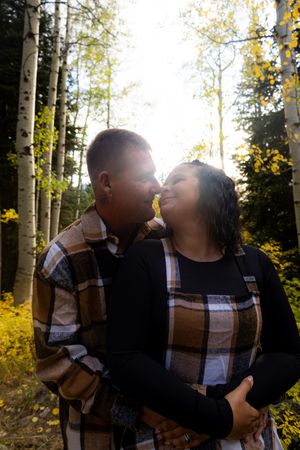 Couple sharing intimate moment among sunlit aspen trees.