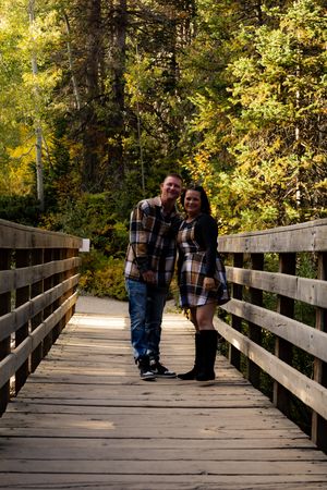 Couple sharing tender moment on wooden bridge surrounded by autumn trees.