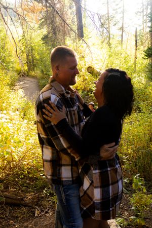 A romantic autumn photoshoot in a sunlit forest with a couple embracing among golden foliage.