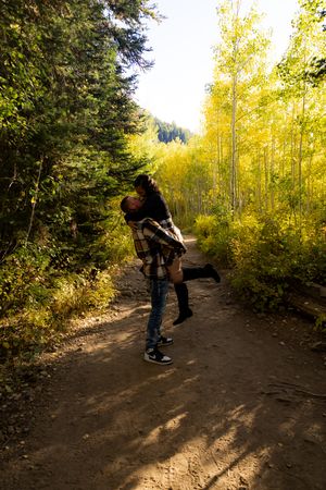 Dancing and twirling together on a dirt path surrounded by golden fall trees.