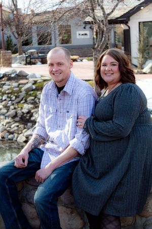 Couple sitting together on stone wall during outdoor photo session.