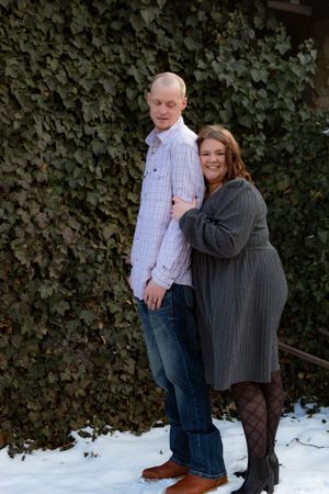 A winter engagement photoshoot with a couple posing against an ivy-covered wall.