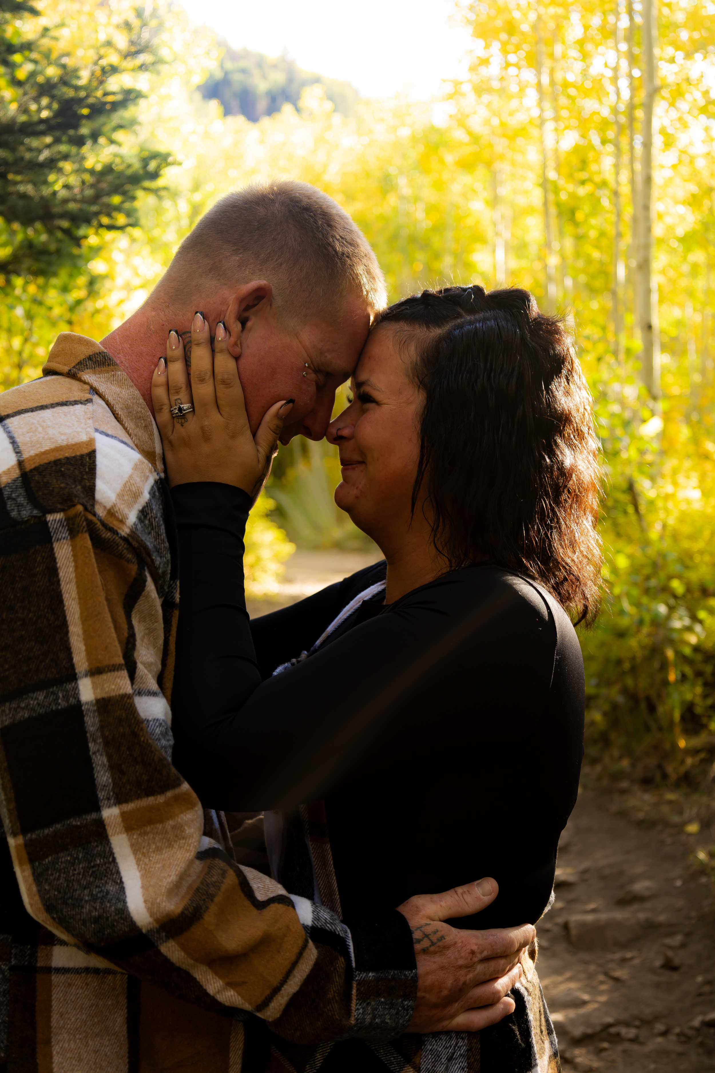 Couple sharing tender moments during a golden hour photoshoot in an autumn forest setting.