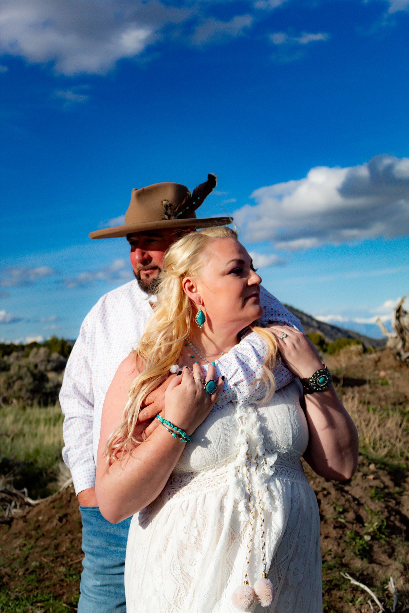 Wedding couple silhouetted against bright blue sky with white clouds.