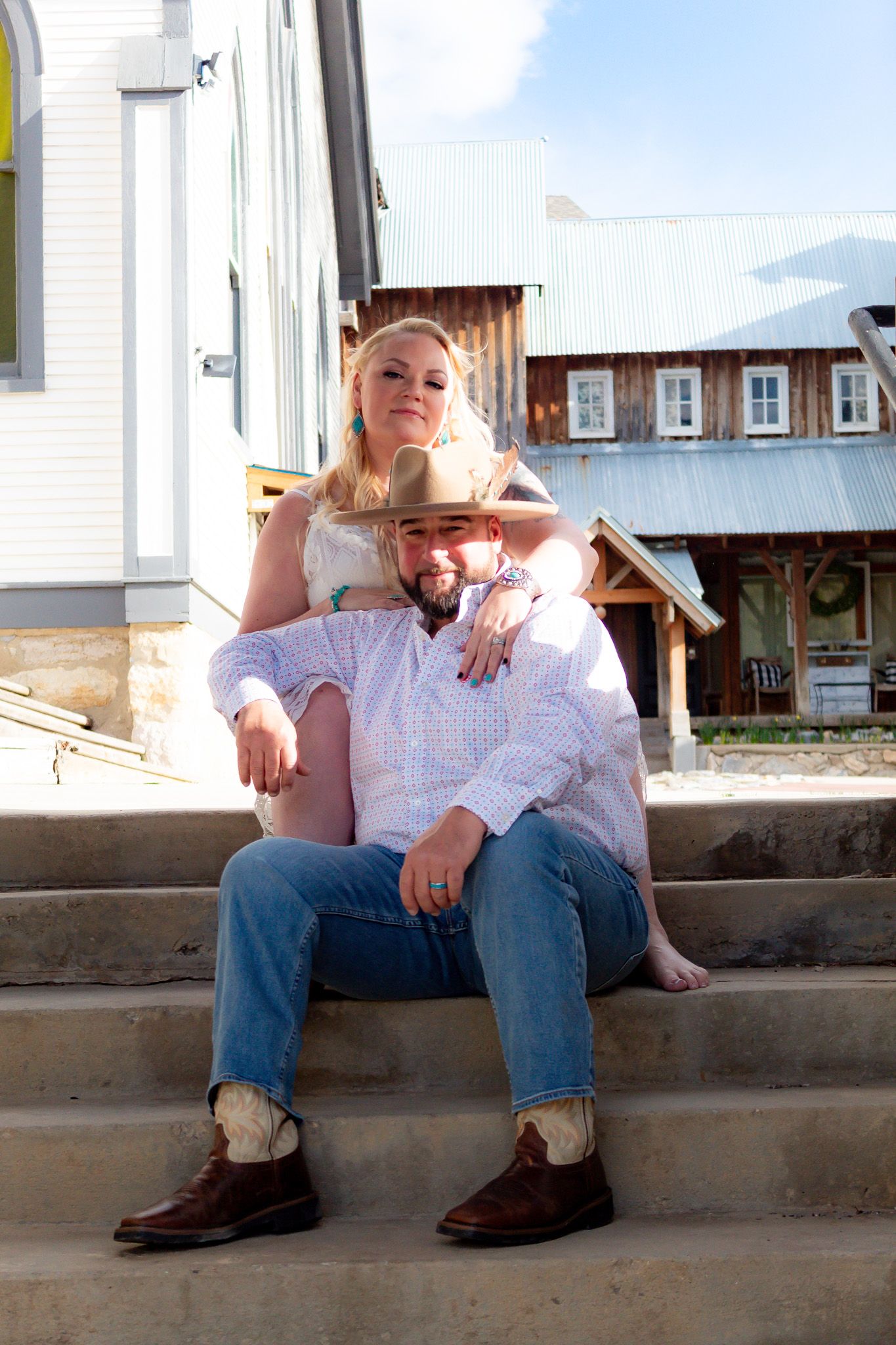 Couple sitting on concrete steps in casual western attire outside a white building.