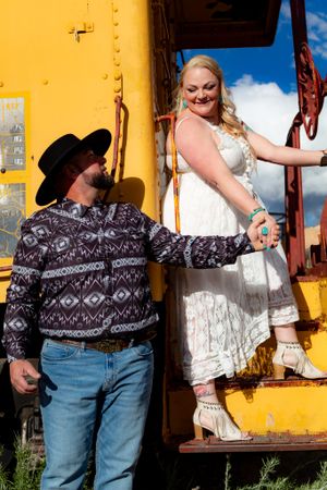 Western-styled couple posing playfully against a bright yellow wall background.