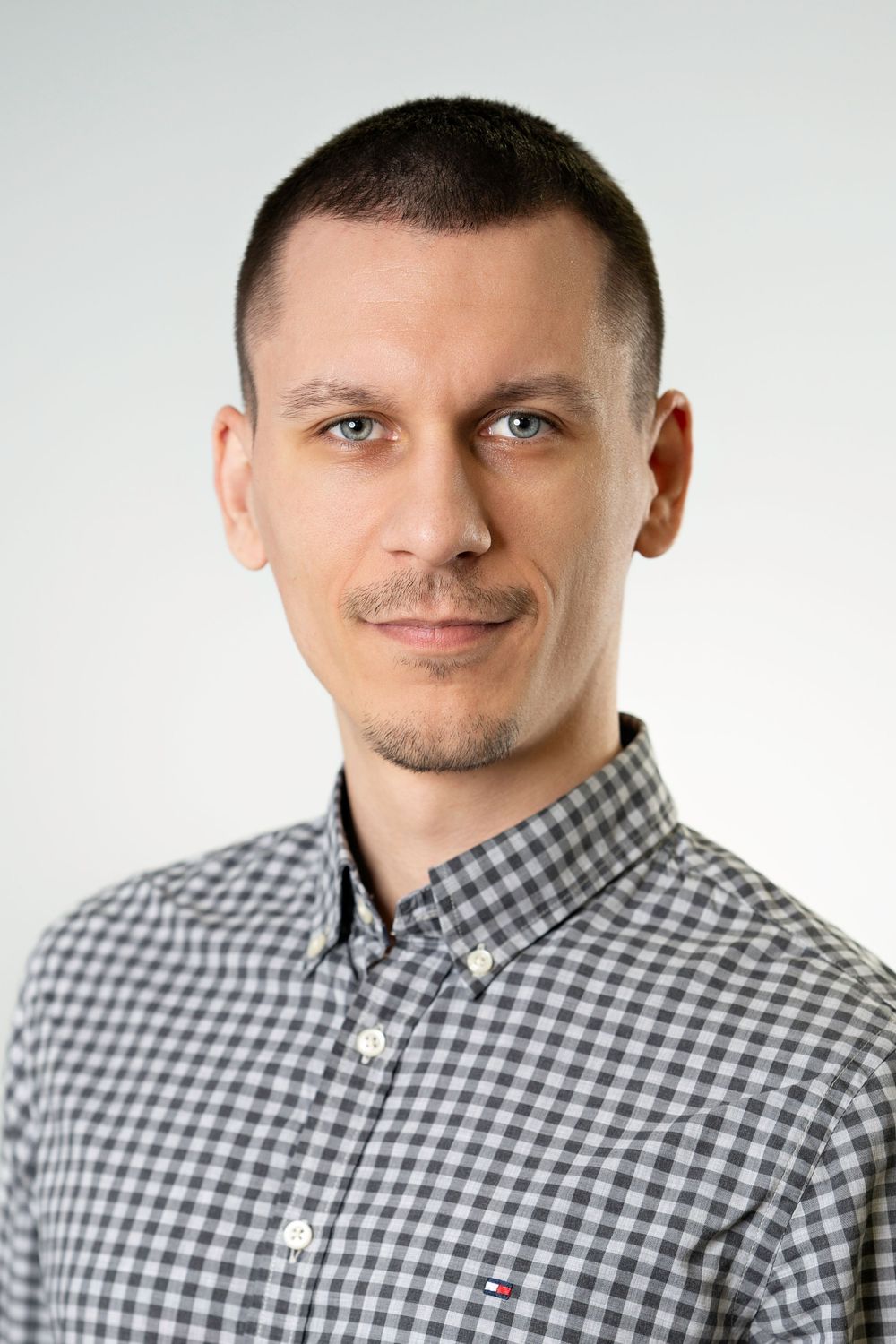Professional headshot of person in checkered button-down shirt against white background.