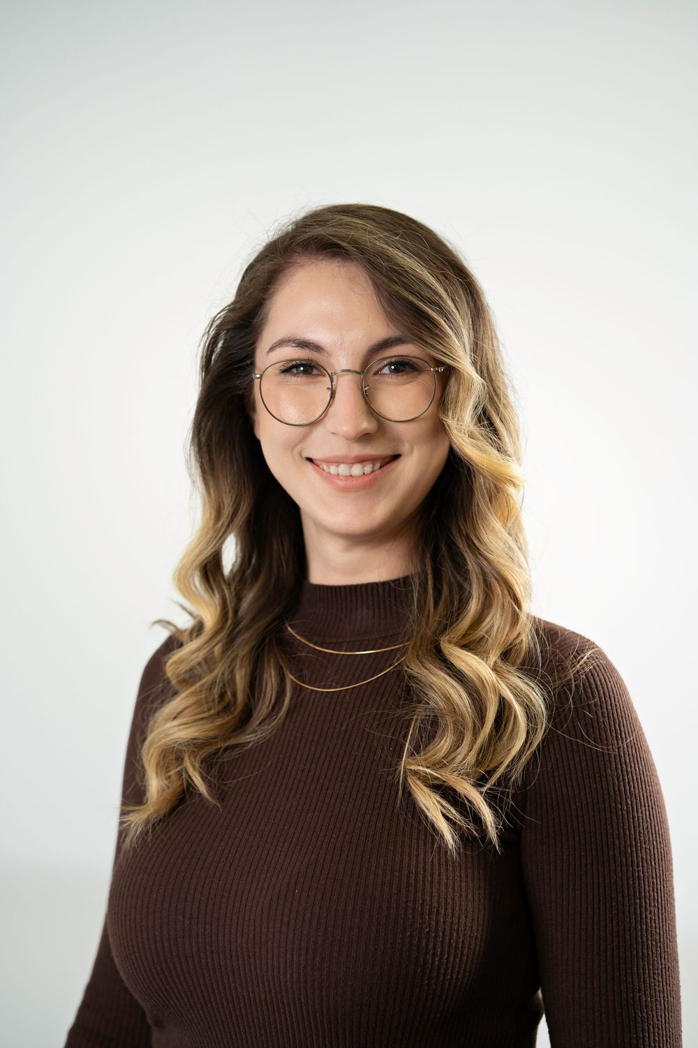 Professional headshot of person with long wavy hair wearing brown turtleneck sweater.