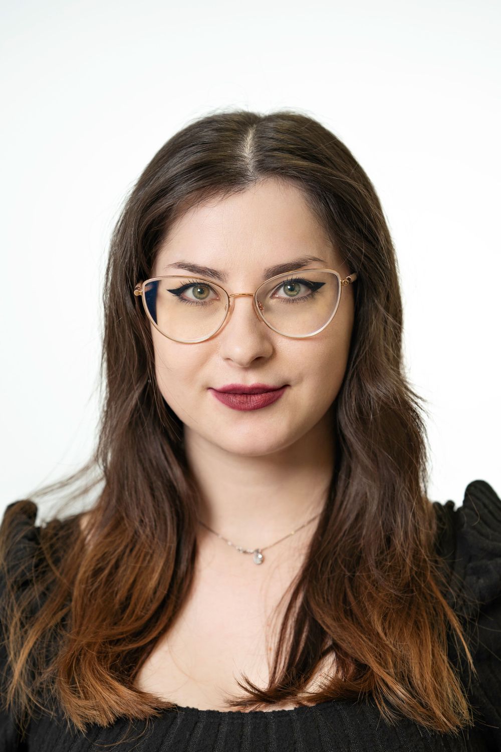 Professional studio portrait of person with glasses wearing dark top against white background.