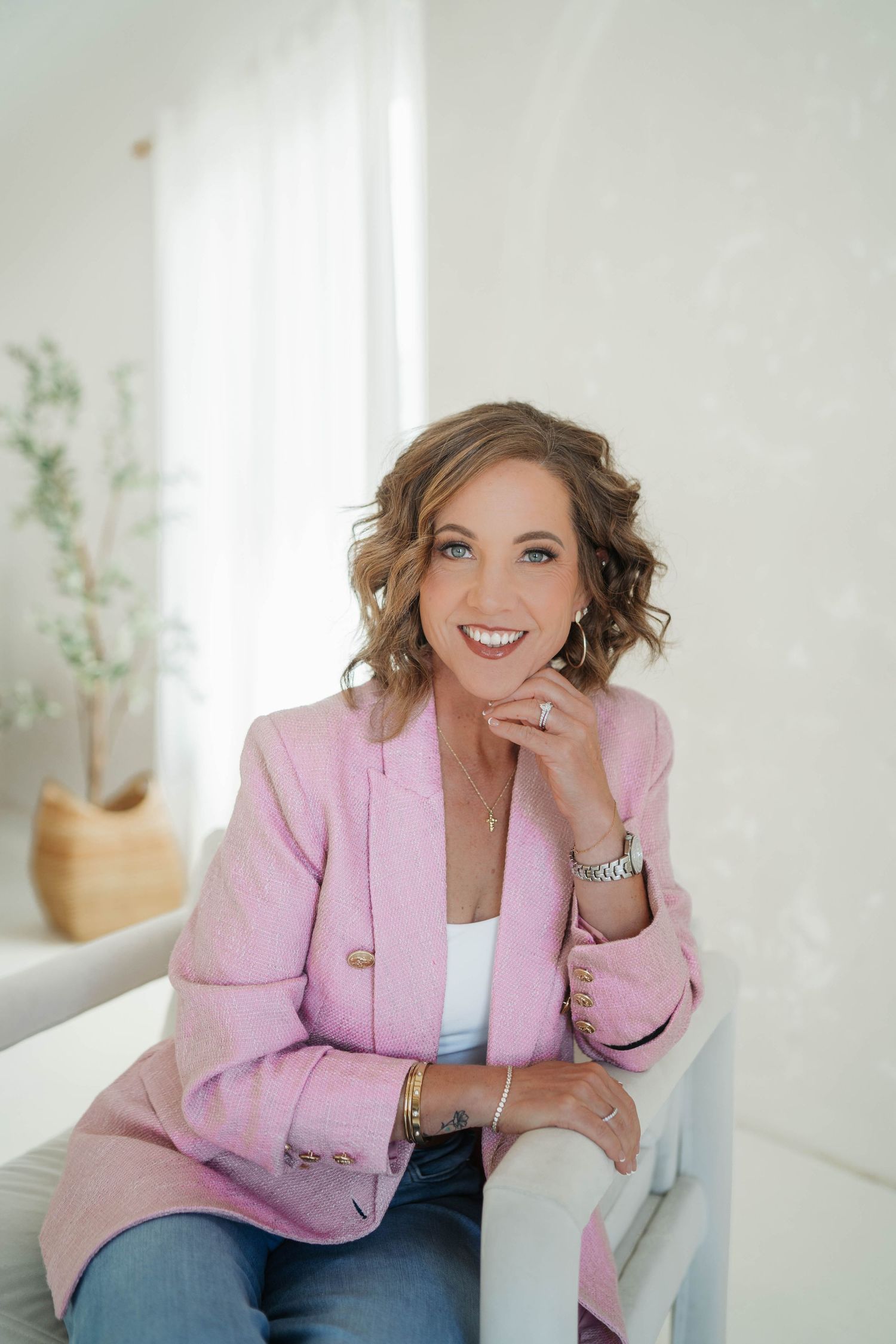 Woman in pink blazer and jeans smiling confidently in bright white modern interior setting.