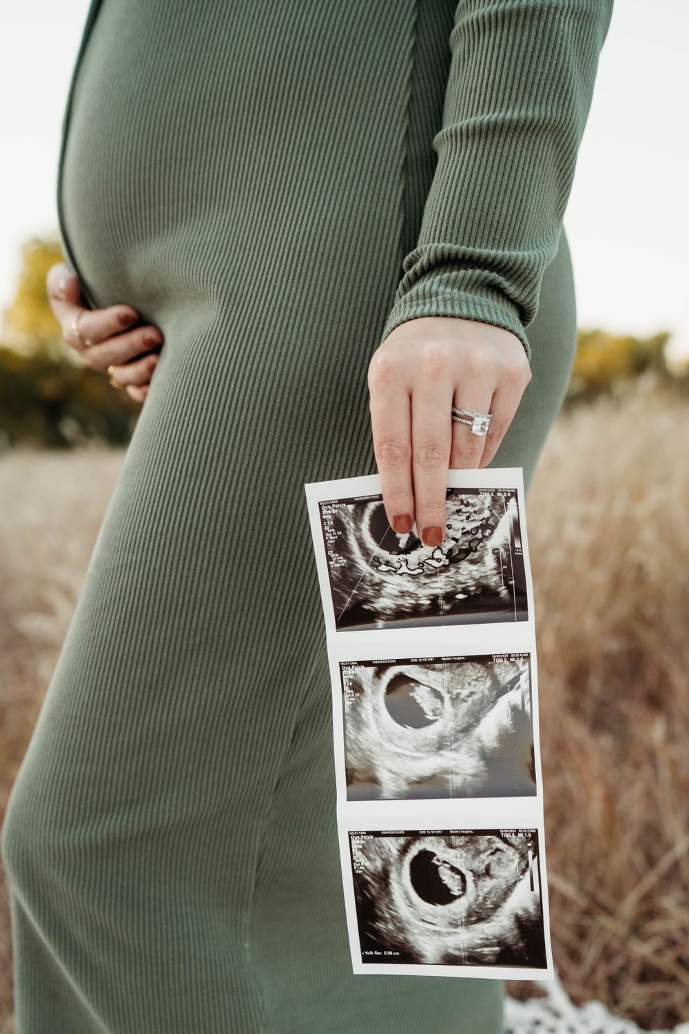 Pregnant woman in green dress holding ultrasound photos during outdoor photoshoot.