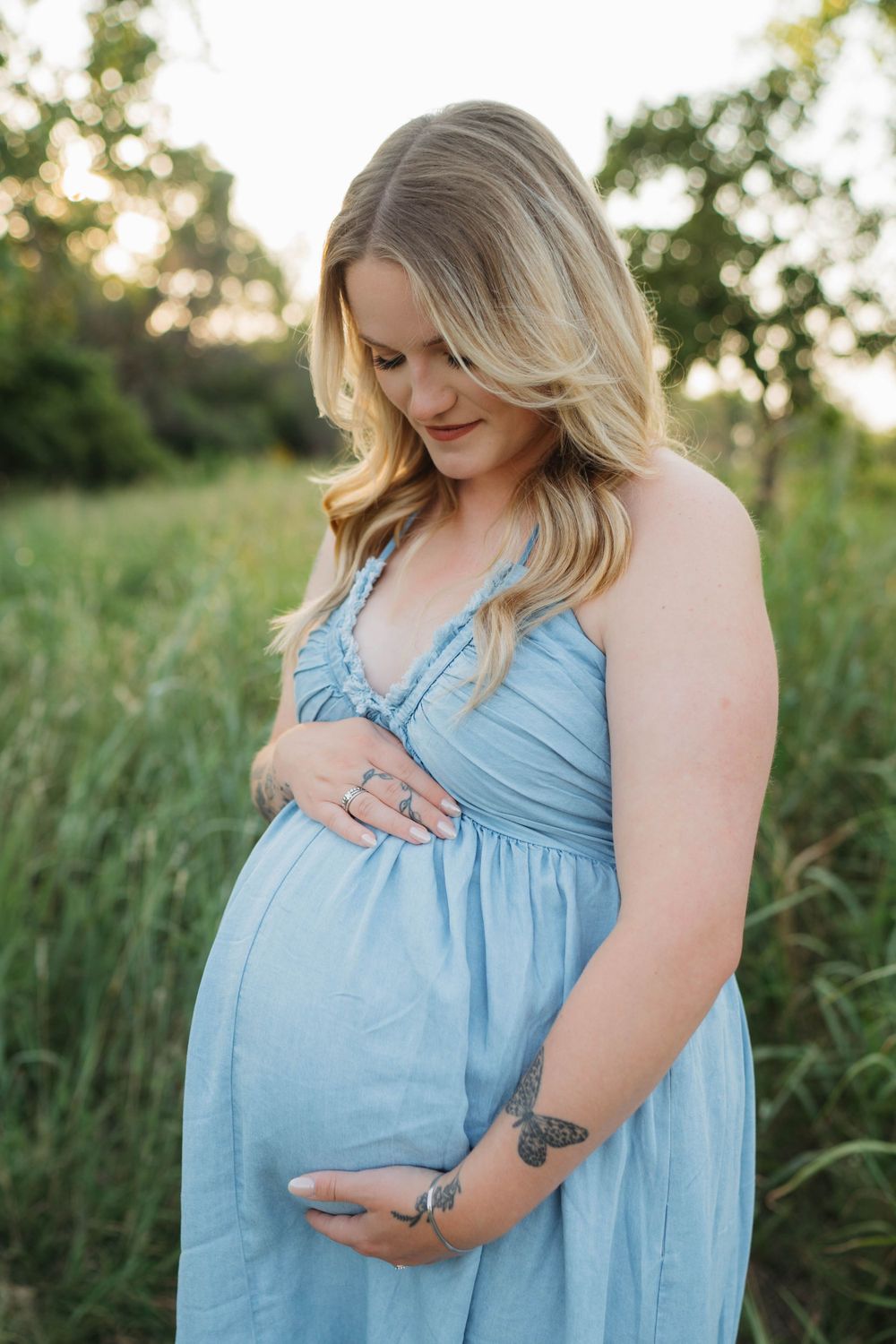 Pregnant woman in light blue dress touching belly during sunset photoshoot.