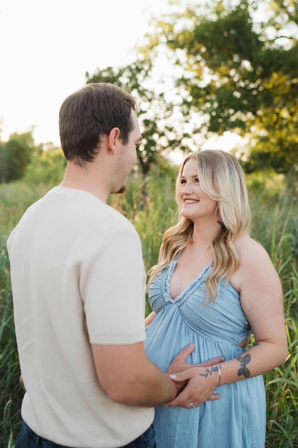 Expecting couple shares a tender moment outdoors at sunset, with the pregnant woman wearing a flowing blue dress.