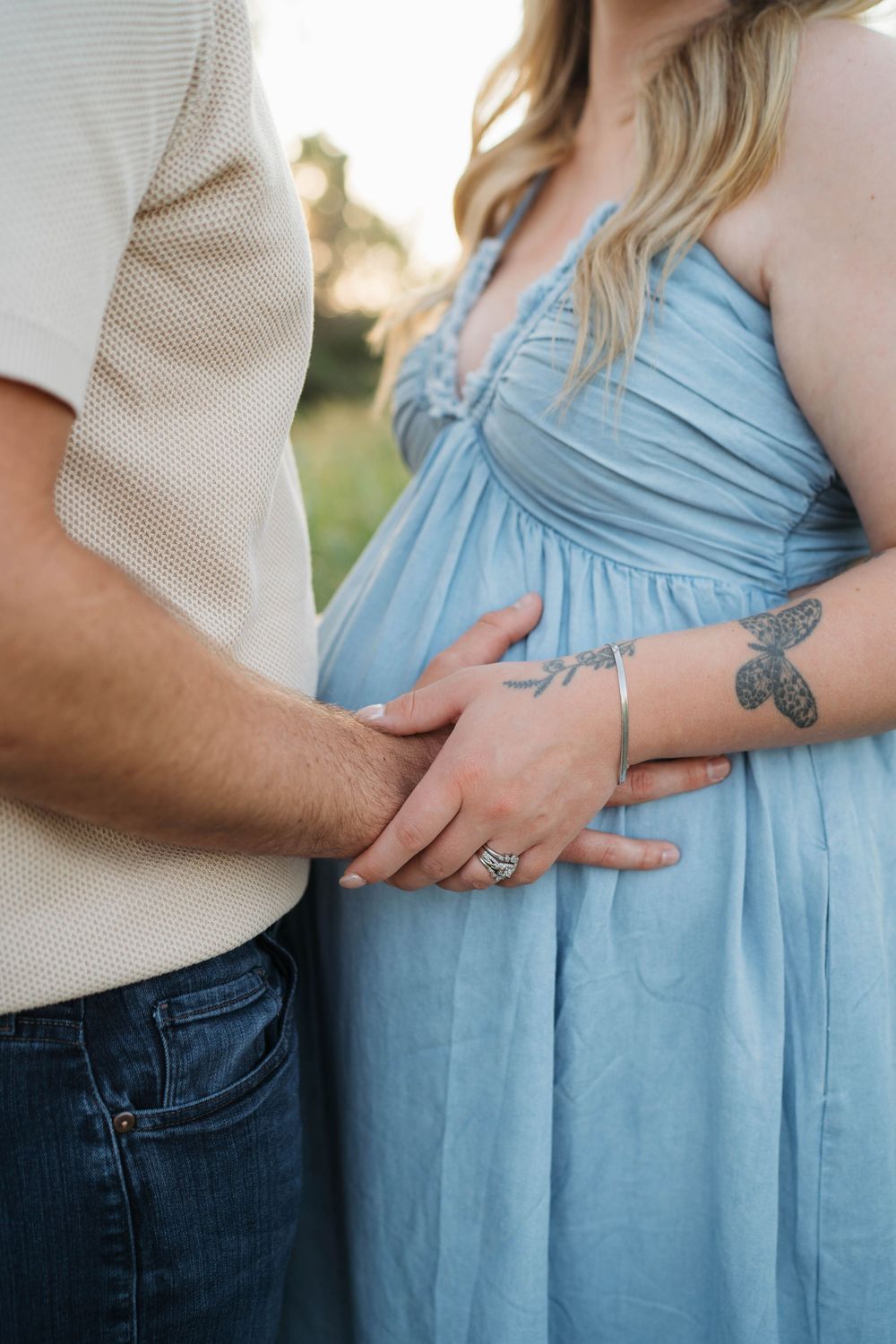 Close up of a couple in a light shirt and flowing blue dress showing a butterfly tattoo on an arm.