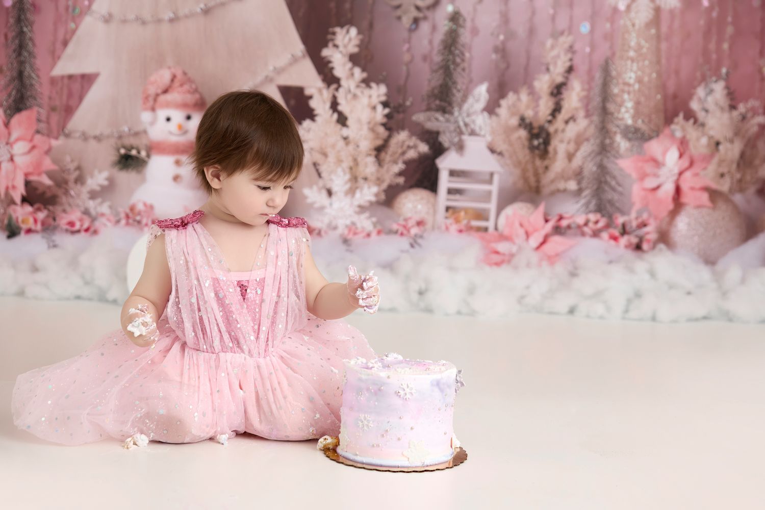 A small figure in pink tutu sits next to cake in dreamy pink winter wonderland setup with white trees and decorations. - Port Chester, NY