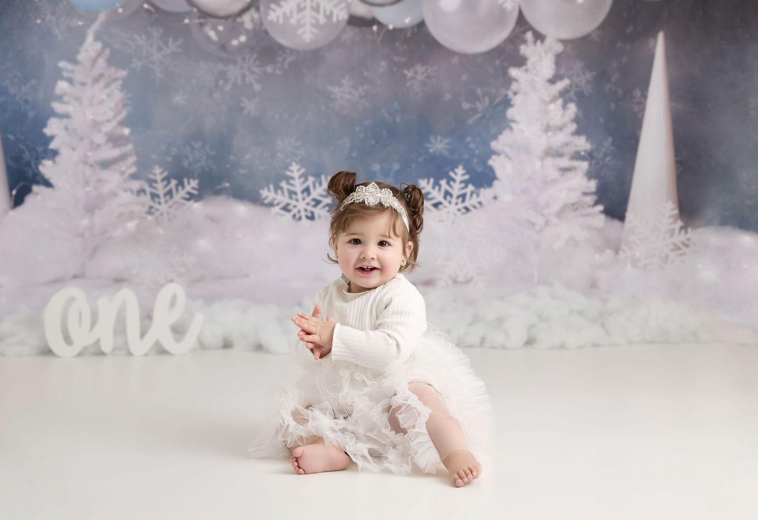 Small child sits in dreamy winter wonderland photo setting with white trees and snowflakes against blue backdrop. Port Chester, NY