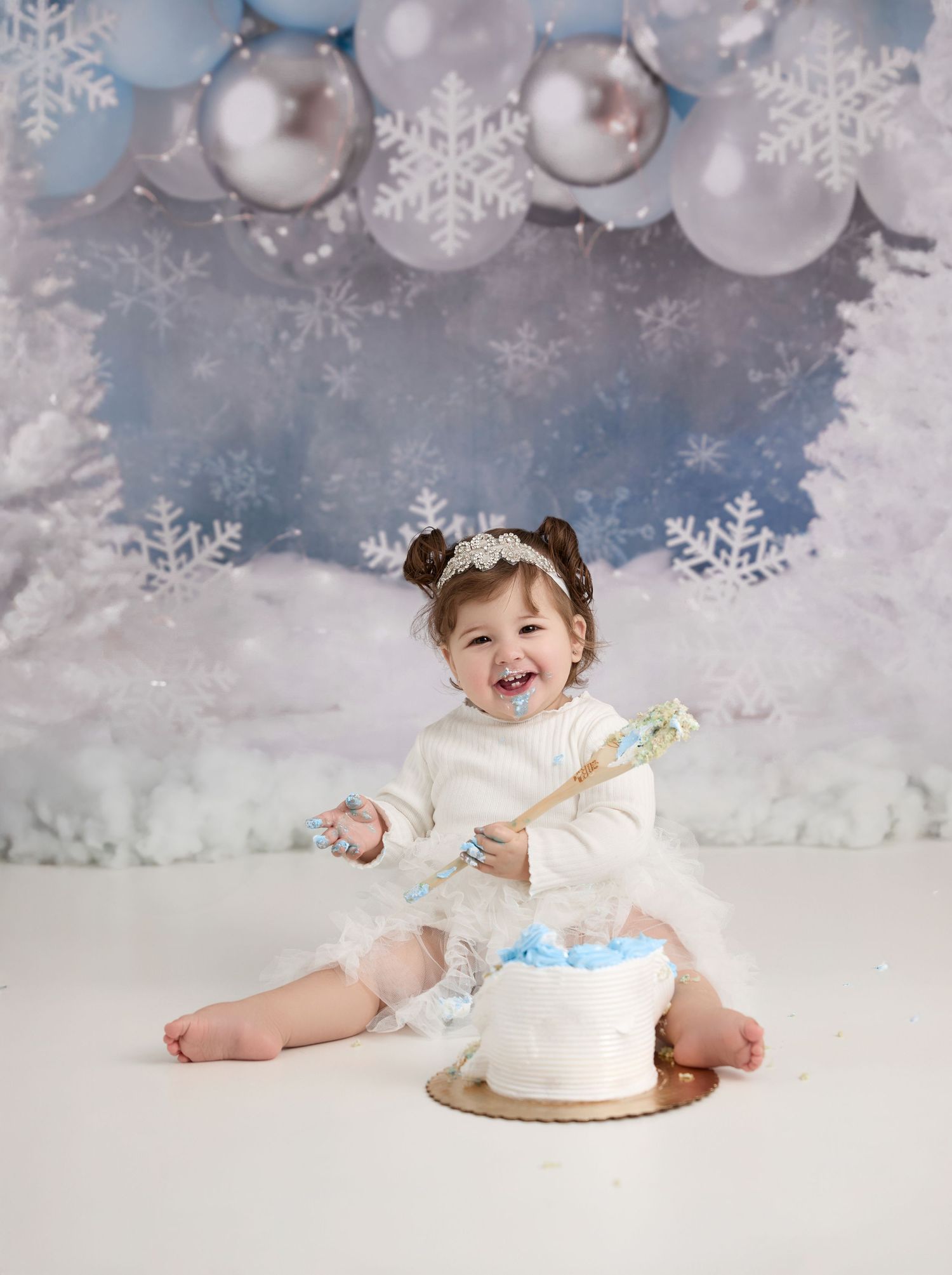 A winter wonderland themed cake smash photoshoot with silver ornaments and snowflakes decorating the set. - Port Chester, NY