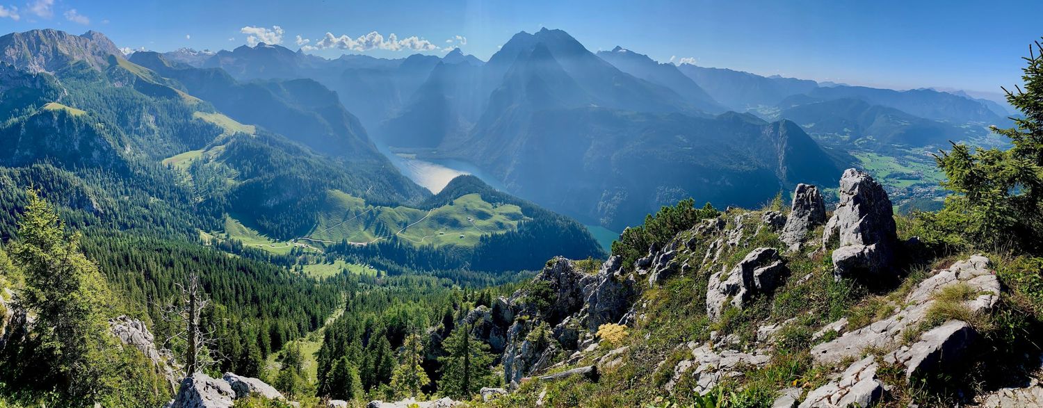 Panoramic view of snow-capped mountain ranges and green valleys in the Alps stretching across the horizon.
