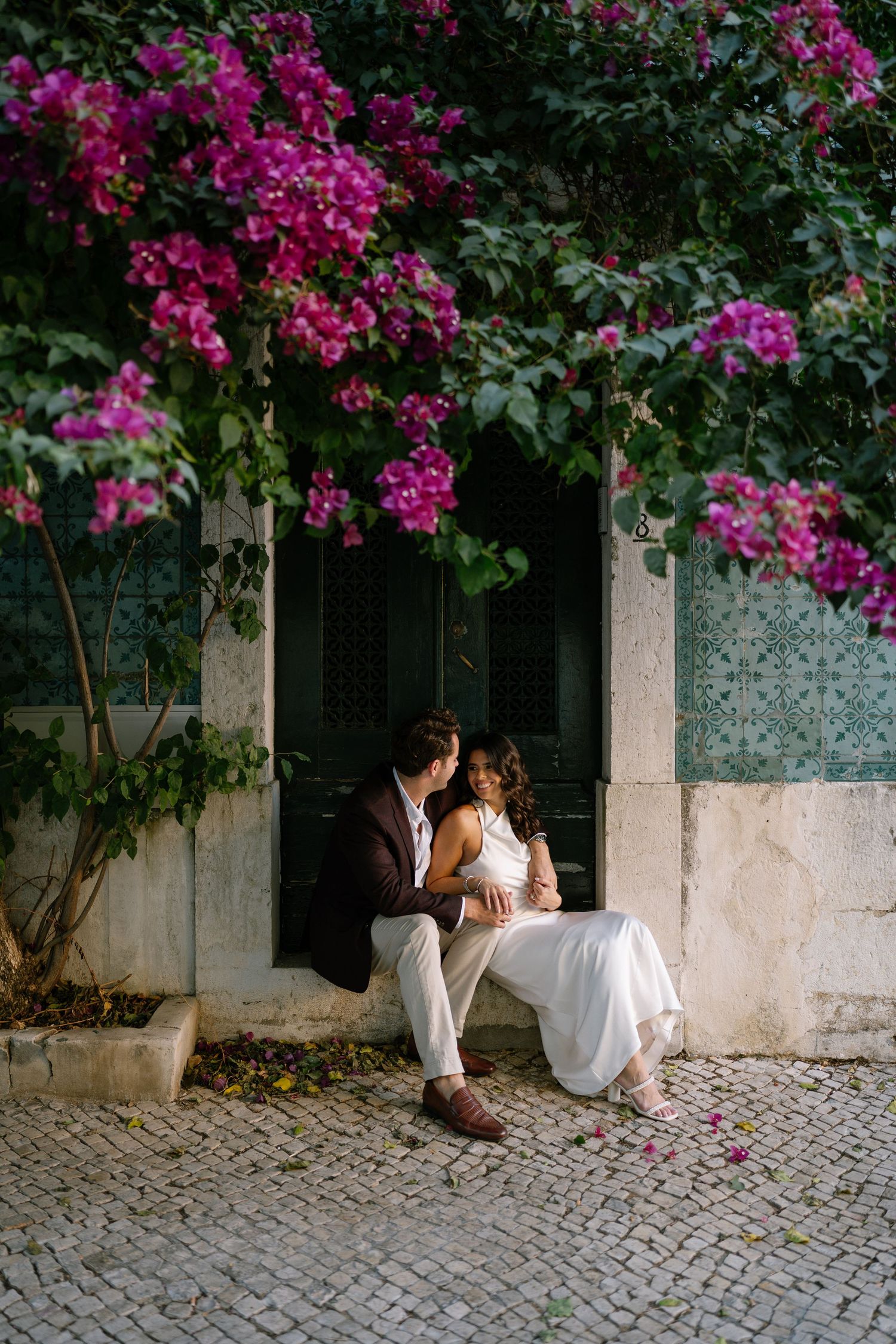 bougainville and blue tiles wall and a couple sitting at the doors of Alfama in Lisbon