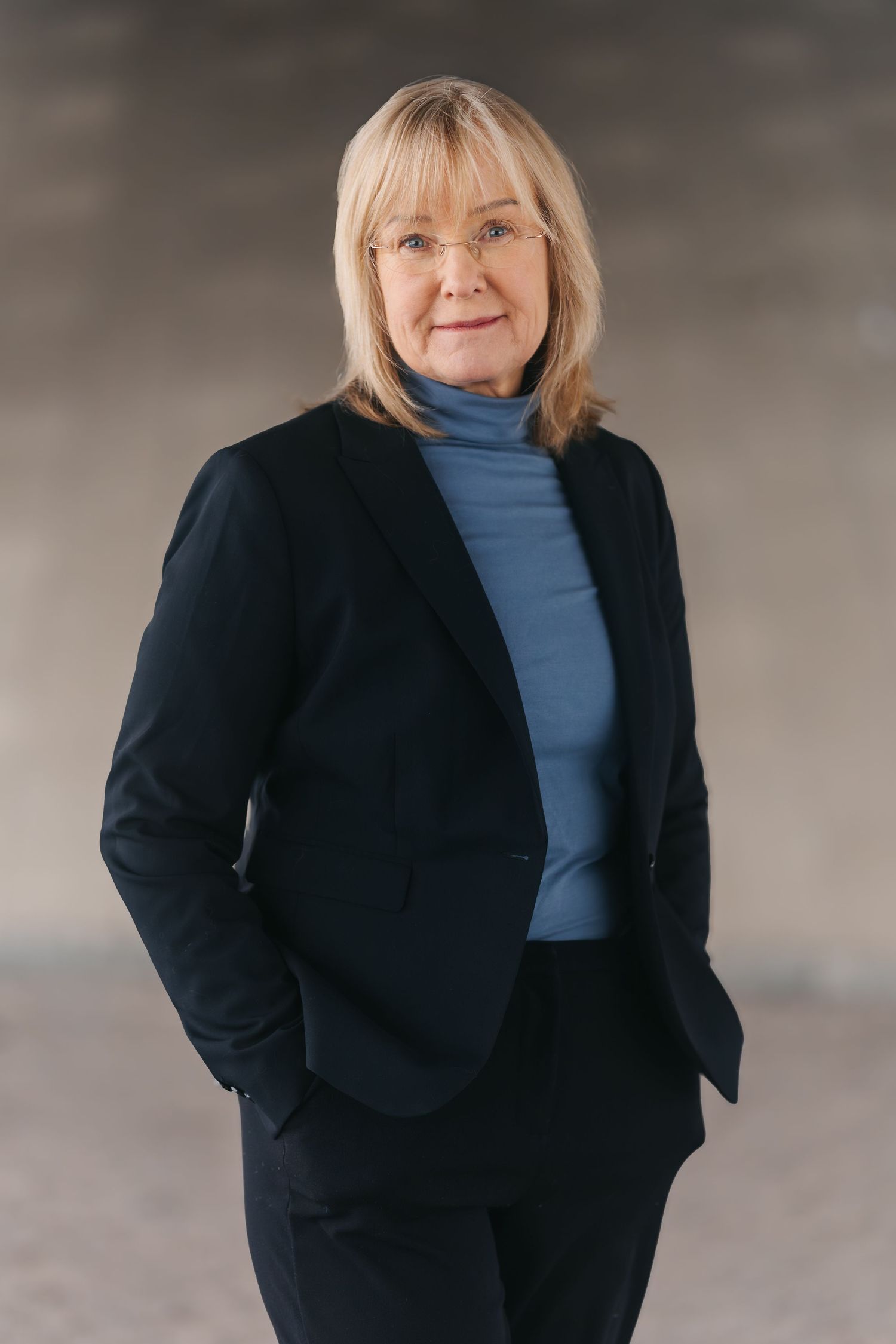 A person in a black blazer and blue turtleneck sweater is shown in a series of similar poses against a gray background.