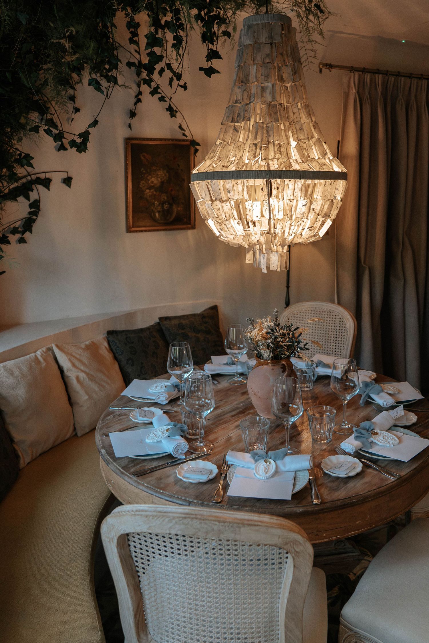 Elegant dining table set with crystal chandelier, white chairs, and table settings in a cozy restaurant interior.