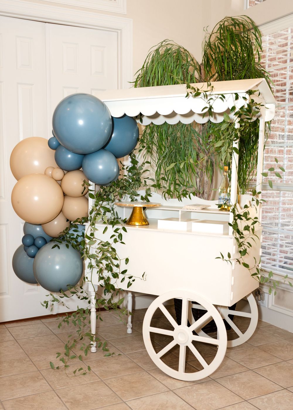 A decorative white cart display with blue and beige balloon arrangements and trailing greenery.