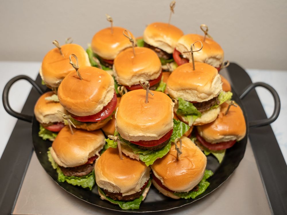 A platter of mini sliders with fresh lettuce and tomatoes arranged on a black serving tray.