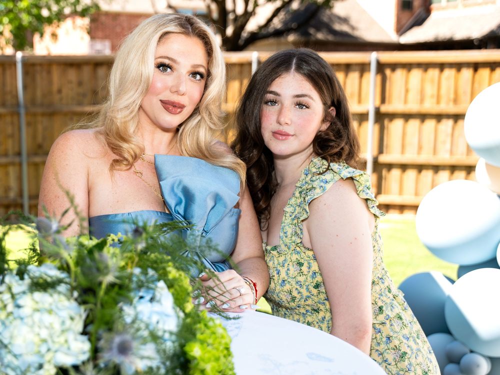 Two women in floral and blue dresses pose together in an outdoor garden setting with hydrangea flowers.