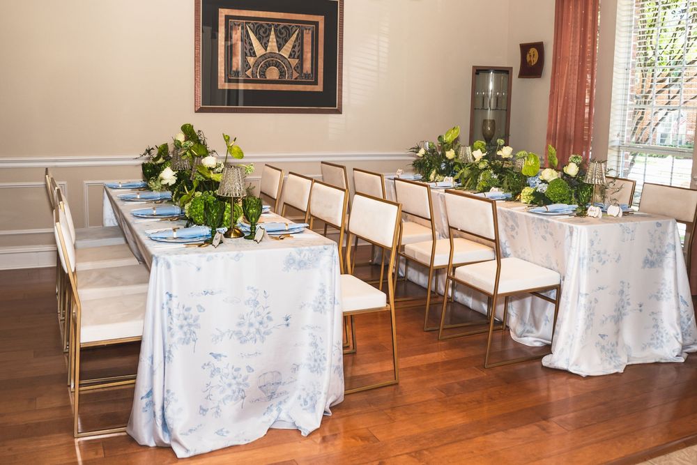 Elegant dining room setup with white tablecloths, gold chairs and green floral centerpieces on hardwood floors.
