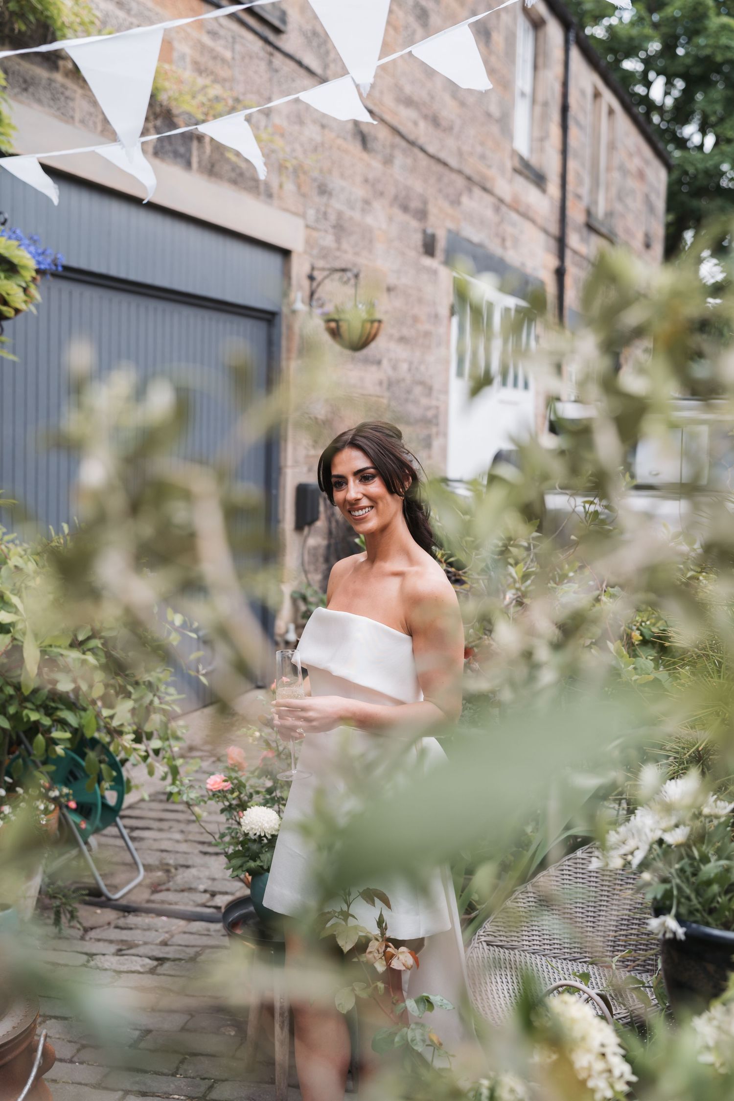 A romantic garden wedding scene with white bunting decorations and stone building backdrop in soft natural lighting.