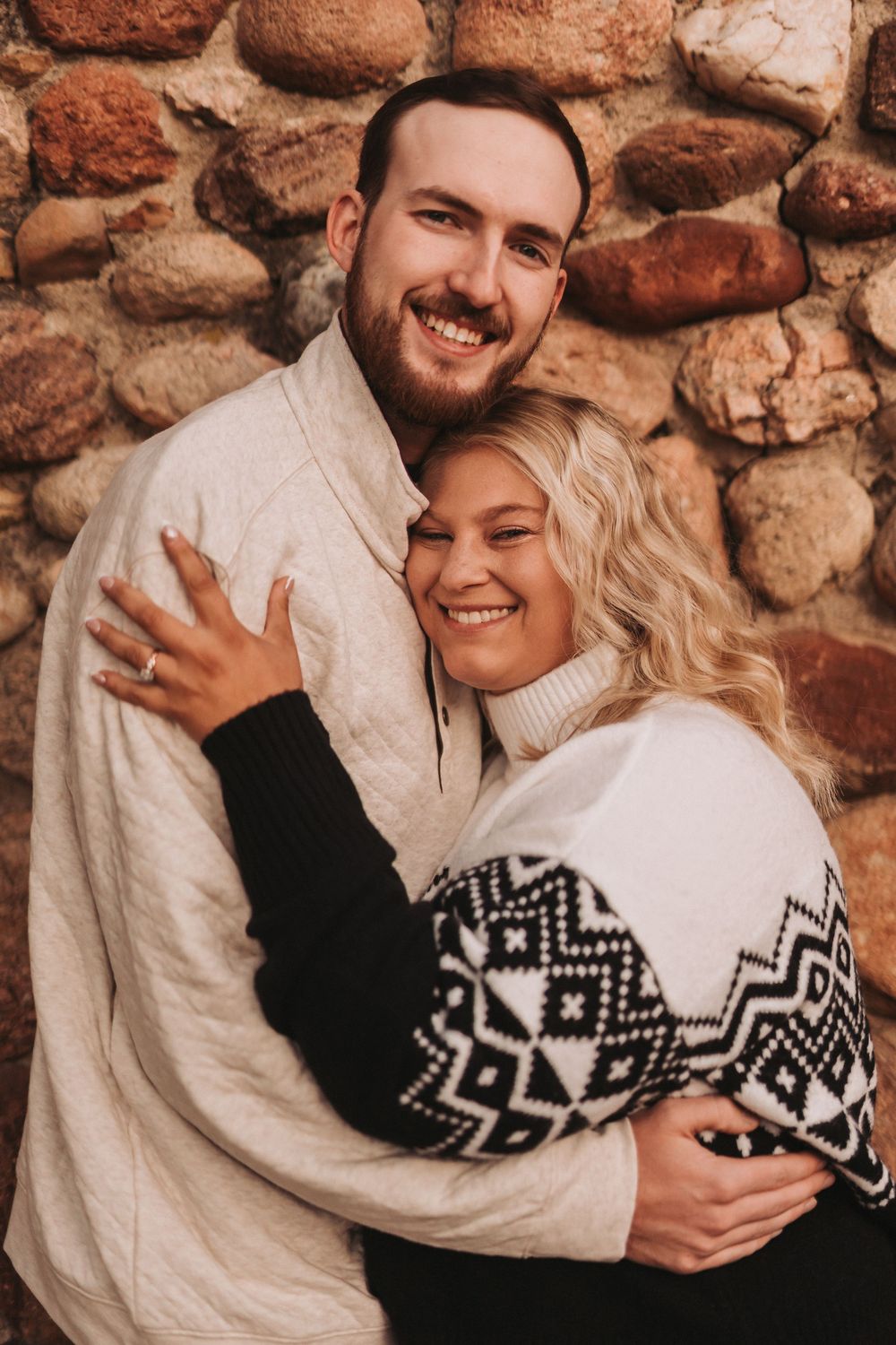 Couple in cozy winter sweaters sharing intimate embraces against rustic stone wall background.