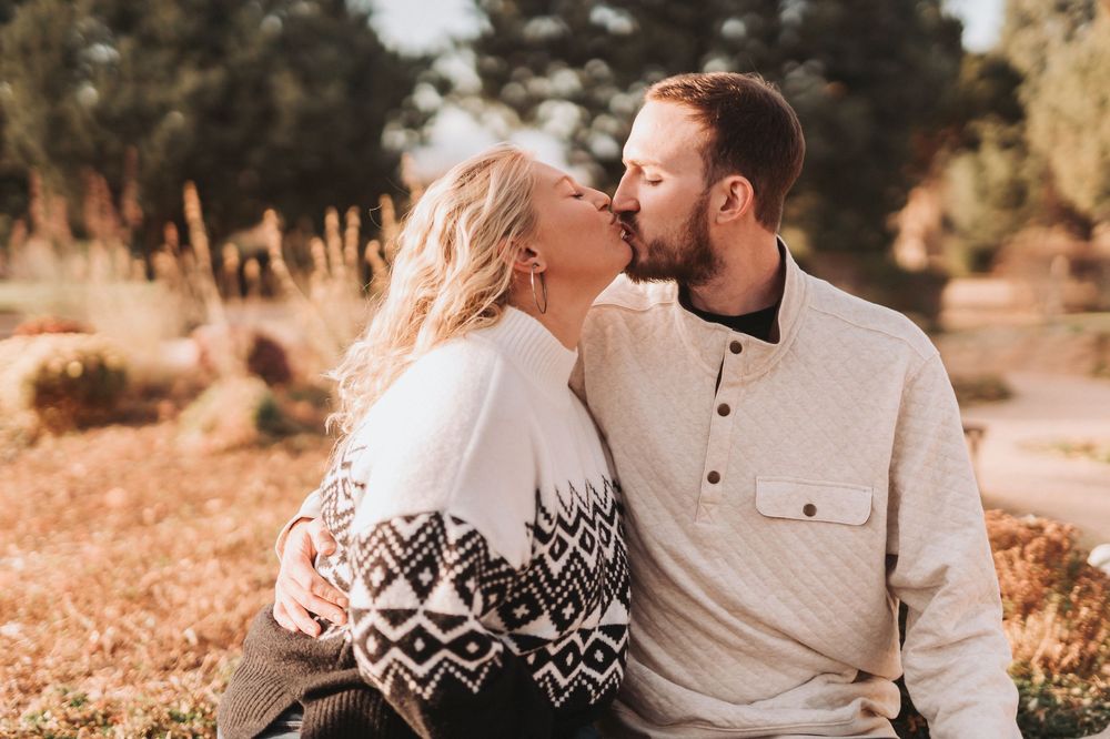 A couple shares a romantic moment in a sun-drenched outdoor setting wearing coordinated neutral and patterned outfits.
