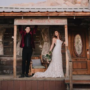 Bride and groom posing on rustic wooden porch of Heartbreak Hotel in desert wedding photo.