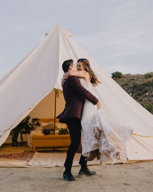 Bride and groom share a romantic kiss outside a white bell tent at their boho desert wedding.